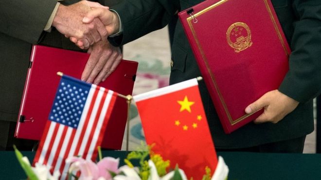 Close up of US and Chinese official shaking hands, holding documents. Flags of both countries in the foreground