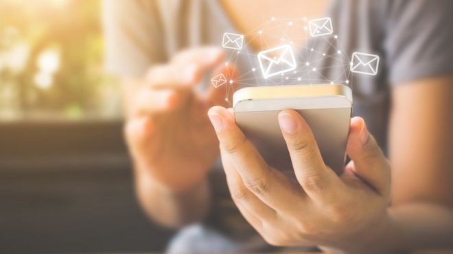 mulher segura um celular na mão; símbolos de mensagem circundam o aparelho