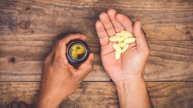 Mano masculina sostiniendo bote con pastillas y píldoras.