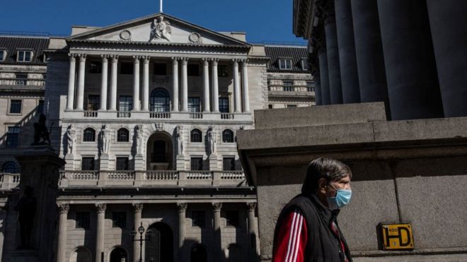 A man wearing a mask walks past the Bank of England in London