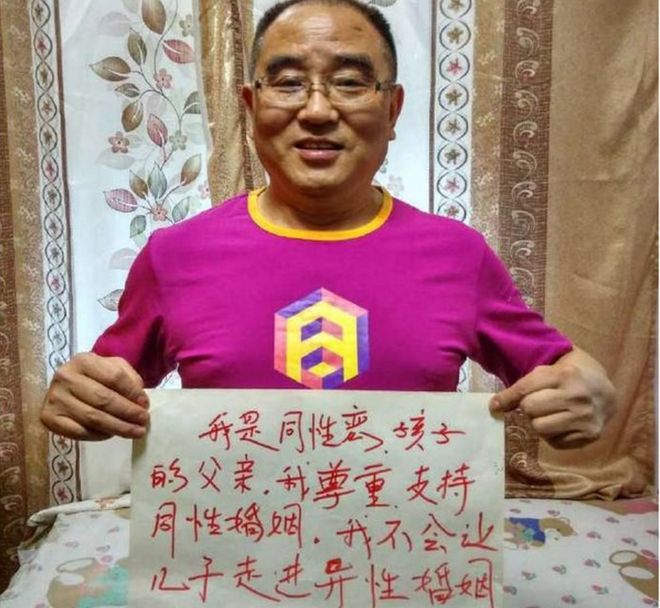 Фотография китайского родителя, держащего табличку с надписью, что они не будут давить на своих детей в браке