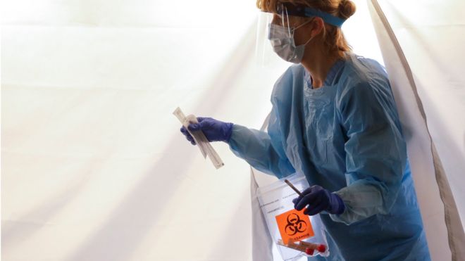 Nurse Becky Barton walks out of a tent with a test kit at a drive-through testing site for coronavirus, flu and RSV, currently by appointment for employees at UW Medical Center Northwest in Seattle, Washington, U.S. March 9, 2020