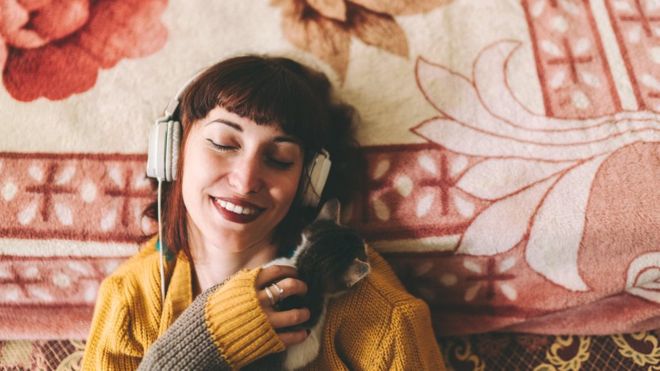 A teenage girl with her eyes closed, hugging a little cat and listening to music