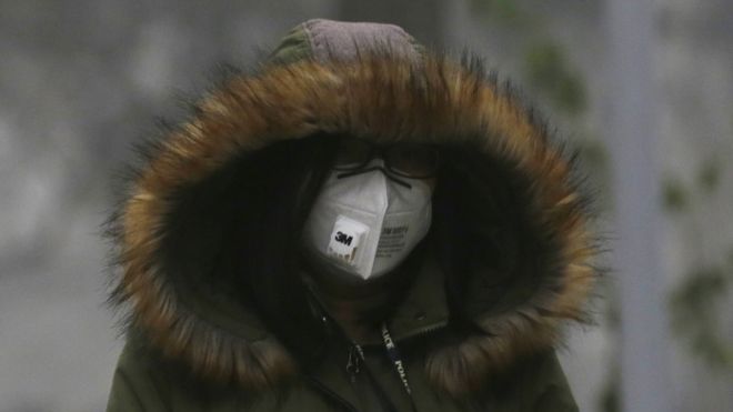 A woman wearing a protective mask and a winter coat walks outside in Beijing