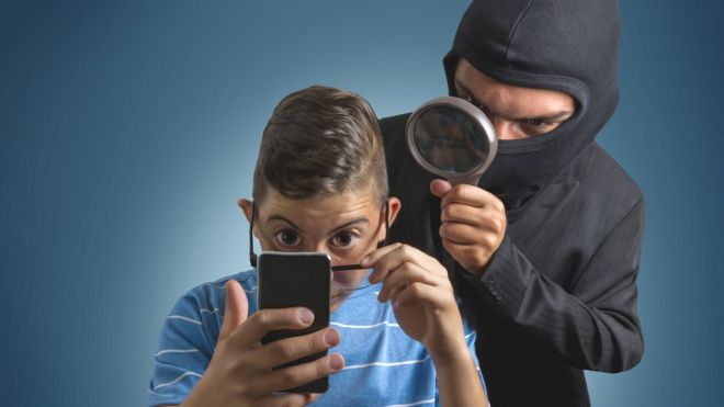 Niño mirando datos en un celular y un ladrón detrás.