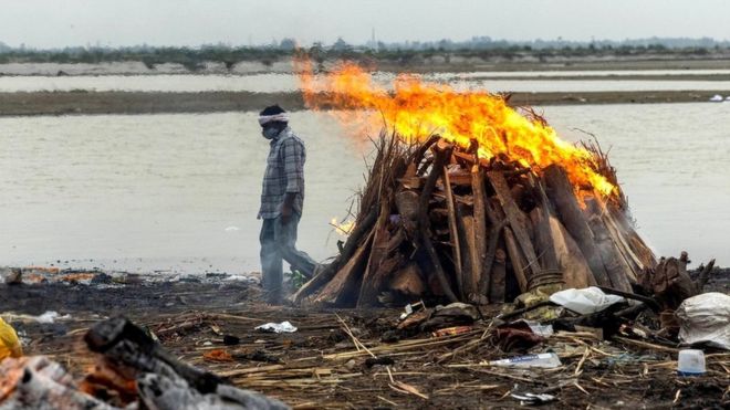 A man walks past burning pyres with people who died from the coronavirus disease (Covid-19), on the banks of the river Ganges in the northern state of Uttar Pradesh