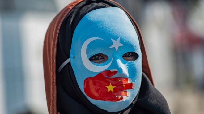 A protester against China's actions in Xinjiang wears a mask with the colours of the flag of East Turkestan