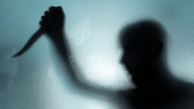 The threatening silhouette of man wielding a knife behind frosted glass window (stock photo)