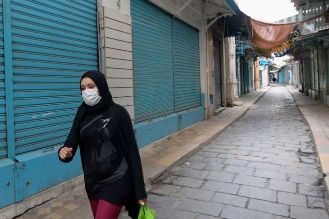 امرأة تونسية ترتدي قناع الوجه الطبي وتسير عبر زقاق خالٍ من الناس في سوق المدينة بتونس،