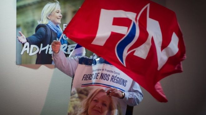 Сторонник развевает флаг Национального фронта рядом с плакатом Марин Ле Пен (28 октября 2015 г.)