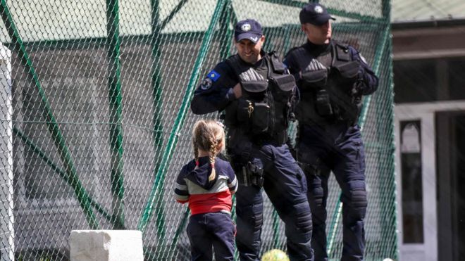 Изображение показывает молодого косовского ребенка, смотрящего на косовских полицейских