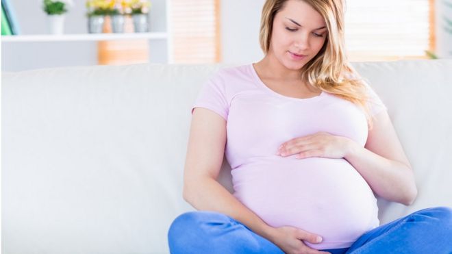 Беременная женщина сидит на диване, держась за живот