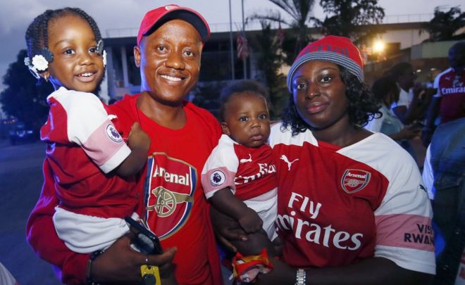 Семья фанатов «Арсенала» позирует фотографу во время прибытия бывшего футбольного тренера Арсена Венгера в международный аэропорт Робертс в Харбеле, Либерия, 22 августа 2018 года.