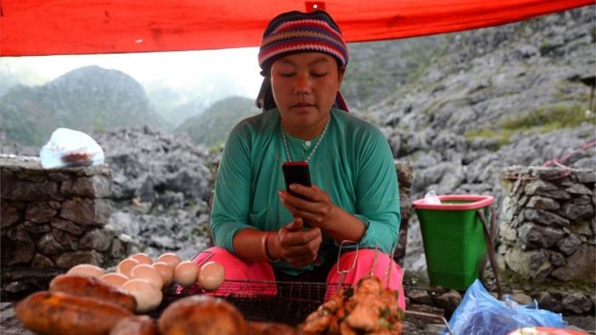 Этническая женщина-хмонг проверяет свой телефон у своего рыночного прилавка (октябрь 2018 года)