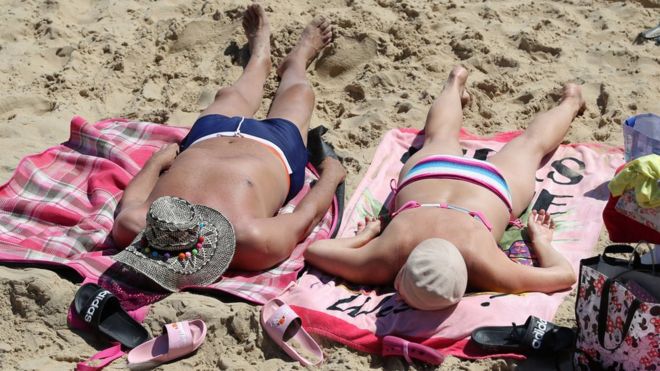 Люди загорают, наслаждаясь теплой погодой на пляже Боскомб в Дорсете
