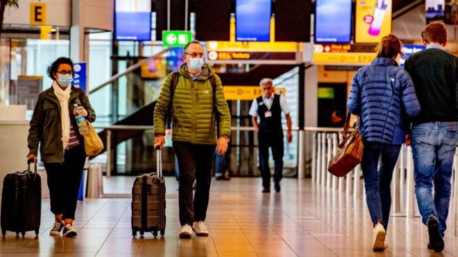 Путешественники в масках в качестве меры предосторожности на стороне KLM в аэропорту Схипхол во время пандемии covid - 19.