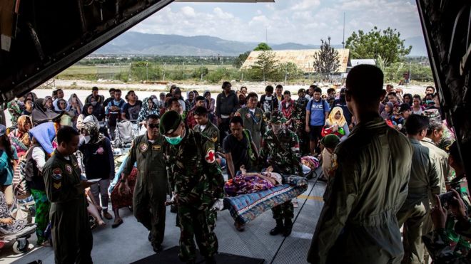Soldiers watch as people board a military plane at Palu airport