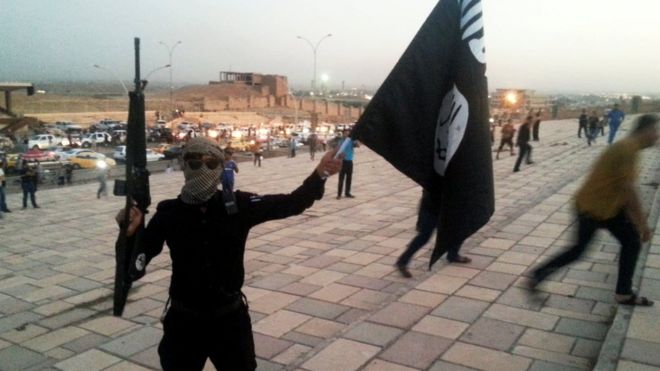 Боец Исламского Государства Ирак и Левант (ИГИЛ) держит флаг ИГИЛ и оружие на улице в городе Мосул, 23 июня 2014 года.