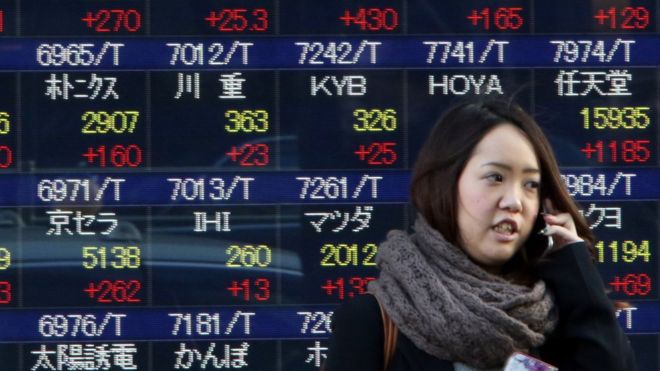 Женщина проходит перед доской цен на акции в Токио 22 января 2016 года.