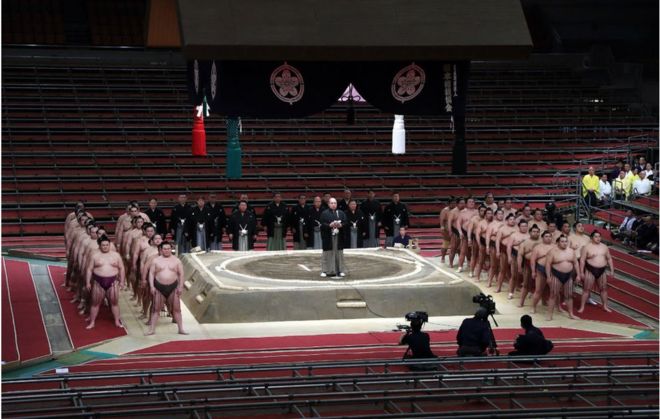 Председатель Ассоциации сумо Хаккаку (C) приветствует борцов сумо во время весеннего грандиозного турнира по сумо, проводимого за закрытыми дверями из-за вспышки коронавируса COVID-19, в Edion Arena Osaka в Осаке 8 марта 2020 г.