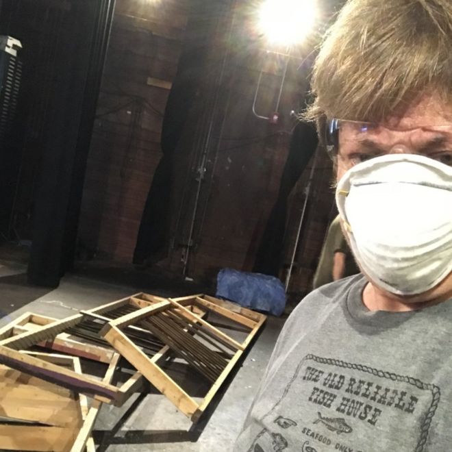 Рея Беккер в маске позирует перед разбитыми предметами мебели