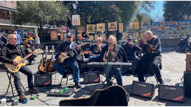 Banda com seis pessoas, duas delas o pastor e sua mulher, tocando em dia de sol na rua