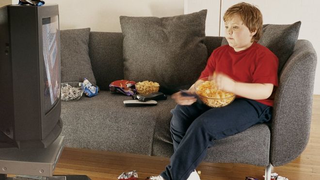 Ребенок смотрит телевизор, ест нездоровую пищу