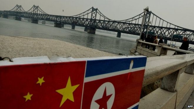 Китайские и северокорейские флаги, прикрепленные к перилам, когда грузовики с китайскими товарами пересекают Северную Корею по мосту китайско-корейской дружбы в китайском пограничном городе Даньдун