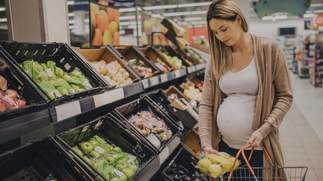 임신한 여성이 슈퍼마켓에서 과일을 고르고 있다