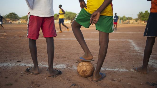 Футболисты бегут за мячом в футбольном матче на футбольном стадионе в районе Танхин в Уагадугу, Буркина-Фасо - сентябрь 2011 г.