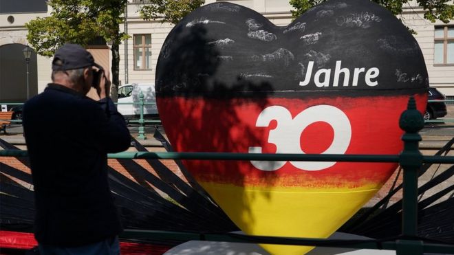 A man photographs a sculpture of a heart in the colors of the German flag that reads: "30 years" in Potsdam
