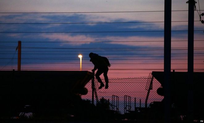 Мигрант, перелезающий через забор на пути к участку Евротоннеля в Кокель в Кале
