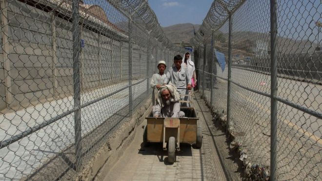Мужчины, прибывающие из Афганистана, движутся по коридору между ограждениями безопасности на пограничном посту в Торхаме, Пакистан, 18 июня 2016 года