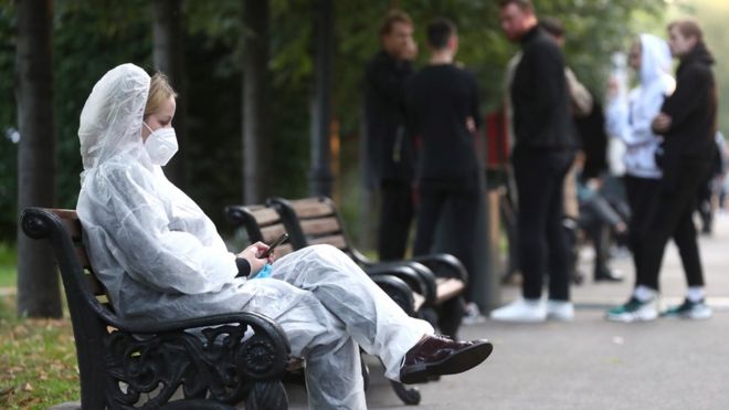 Девушка в защитном костюме на скамейке на одной из улиц Москвы