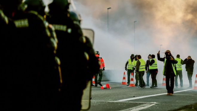 Люди стоят перед жандармами на кольцевой дороге Кана 18 ноября 2018 года в Кане, на северо-западе Франции, на второй день действий после общенационального народного инициированного дня протеста под названием «желтый жилет». (Gilets Jaunes по-французски) движение