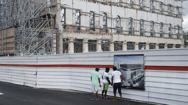 Мужчины останавливаются, чтобы посмотреть на плакат с концептуальным изображением нового отеля, который будет построен вдоль Пасео-де-Марти, широкого бульвара, проходящего через сердце исторического района Старая Гавана (20 марта 2016 года)