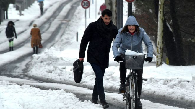 A pedestrian and a cyclist travel along a snow-covered street in Montpellier, southern France, on March 1, 2018