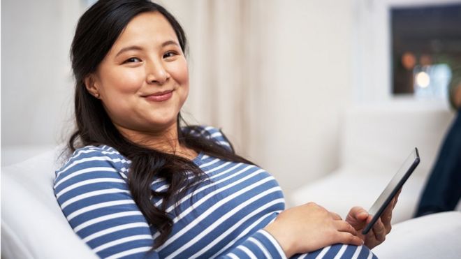 Беременная женщина Азии, глядя на планшет