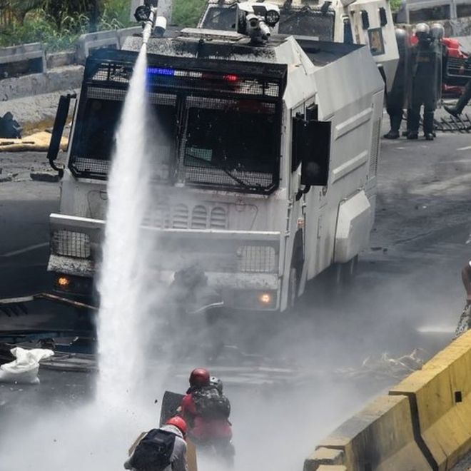 Активисты оппозиции сталкиваются с полицейской водяной пушкой во время акции протеста против президента Венесуэлы Николаса Мадуро в Каракасе (3 мая 2017 г.)