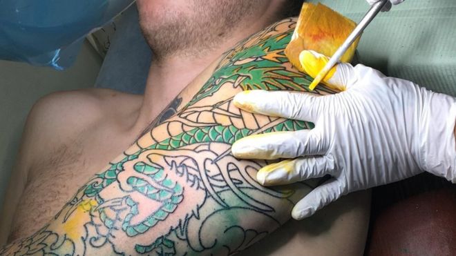 Horimitsu adds yellow ink to the tattoo using a stick tipped with needles