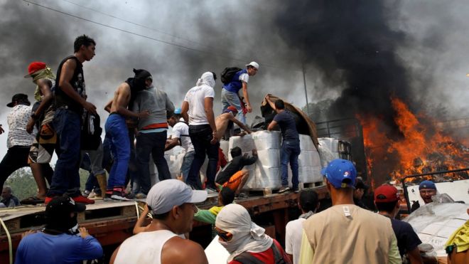 Сторонники оппозиции выгружают гуманитарную помощь из грузовика, который был подожжен после столкновений между сторонниками оппозиции и силами безопасности Венесуэлы на мосту Франсиско де Паула Сантандер на границе между Колумбией и Венесуэлой, как видно из Кукуты,