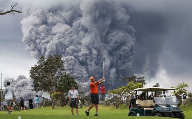 People play golf as an ash plume rises in the distance from the Kilauea volcano on Hawaii's Big Island