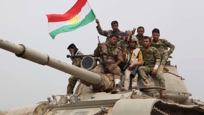 Курдские силы сидят на вершине танка, размахивающего курдским флагом после захвата города Башир 1 мая 2016 года