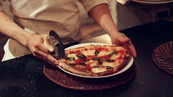 Сотрудник Pizza 4Ps разрезает пиццу