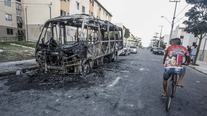 Homem passa de bicicleta ao lado de um micro-ônibus incendiado em Fortaleza, em 4 de janeiro