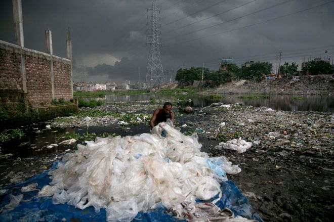 رجل يزيل الأكياس البلاستيكية المعالجة كيميائياً في قناة تؤدي إلى نهر بوريجانجا في دكا، بنغلاديش