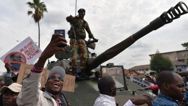 Мужчина делает селфи солдата Зимбабвийских сил обороны, стоящего на танке во время марша по улицам Хараре