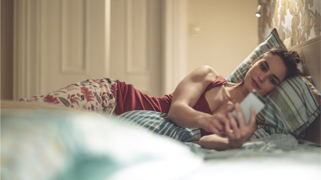Женщина делает покупки в Интернете по мобильному телефону, лежа в постели