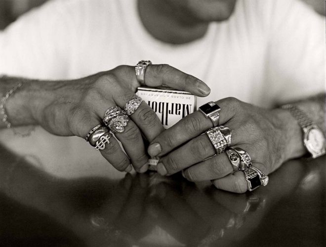 Мужчина с большим количеством колец на пальцах сжимает пачку сигарет