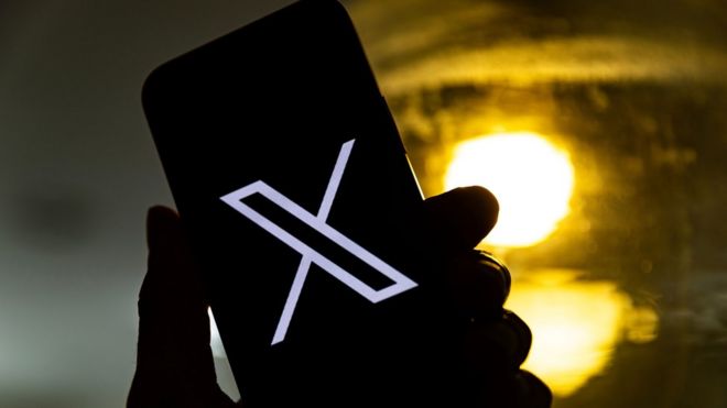 A hand holding a phone with the X logo